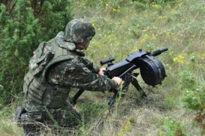 Vojinik okrenut leđima u maskirnoj uniformi podešava Automatski bacač granata M93 na travnatoj površini