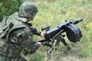 Osoba u maskirnoj uniformi koristi Automatski bacač granata M93 na travnatoj površini